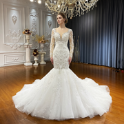 Front view of an elegant mermaid bridal gown on a model featuring a high-quality puffy skirt, long lace sleeves, and an intricately beaded bodice.