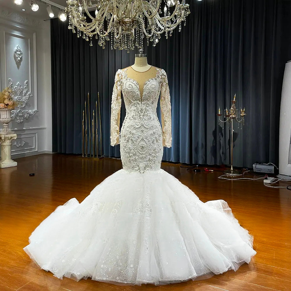 Full-length front view of a stunning mermaid bridal gown with a high-quality puffy skirt and shimmering beaded embroidery under a showroom chandelier.