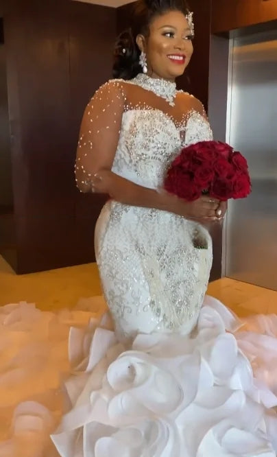 Beautiful African bride posing in a high-neck wedding dress with a heavily beaded collar and shimmering silver details, holding a classic bouquet of red roses.