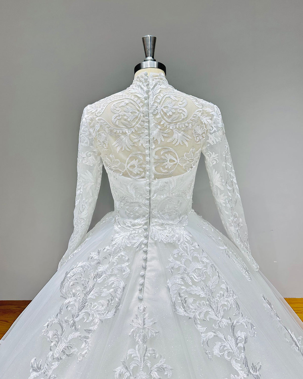 Close-up of the back of a high-neck wedding dress showcasing sheer illusion mesh, floral lace appliques, and a vertical row of fabric-covered bridal buttons over a zipper closure.