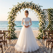 Smiling bride wearing a modest high-neck long-sleeve A-line wedding dress with a sequin-embellished bodice and soft tulle skirt under a beach wedding arch.