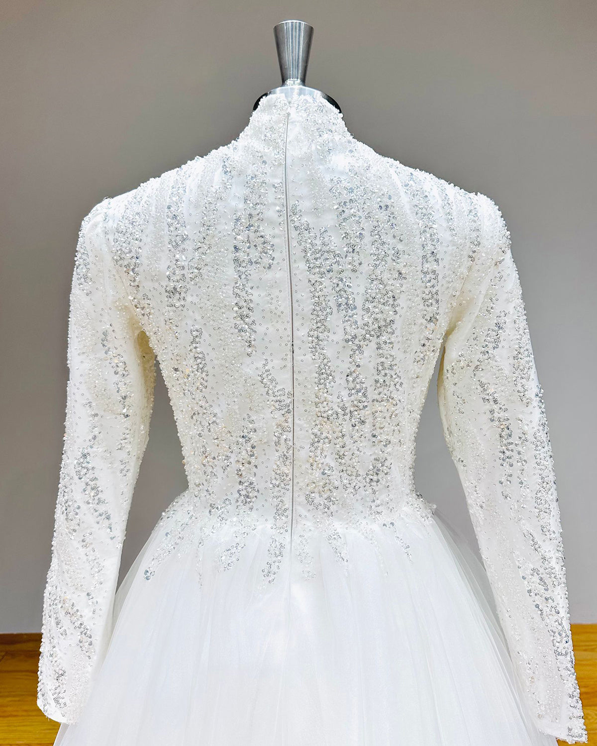 Close-up of the back of a modest bridal dress showing a sleek zipper back closure integrated into a high-neck bodice covered in vertical sequin trails.