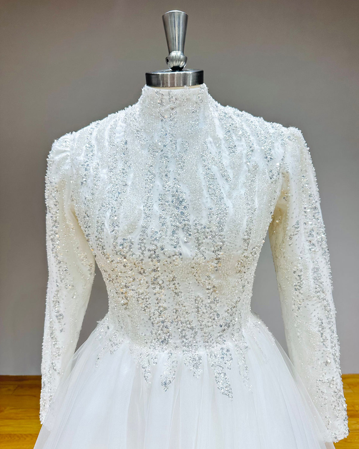 Detailed view of a high-neck bridal bodice emphasizing the dense, textured silver beadwork, shimmering sequins, and structured long sleeves.