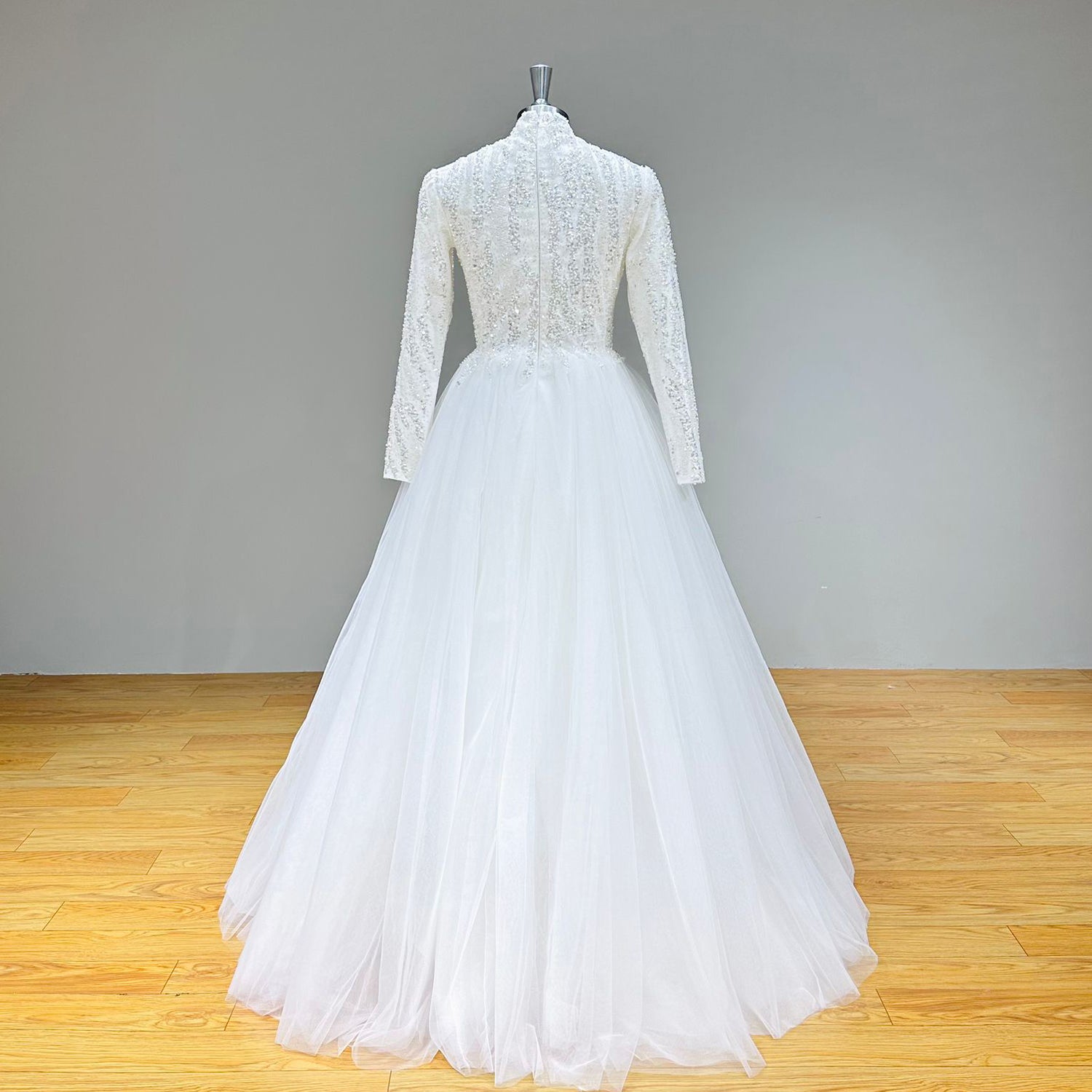 Full back view of a high-neck long-sleeve wedding gown showcasing a clean zipper closure and a floor-length, unadorned tulle A-line skirt.