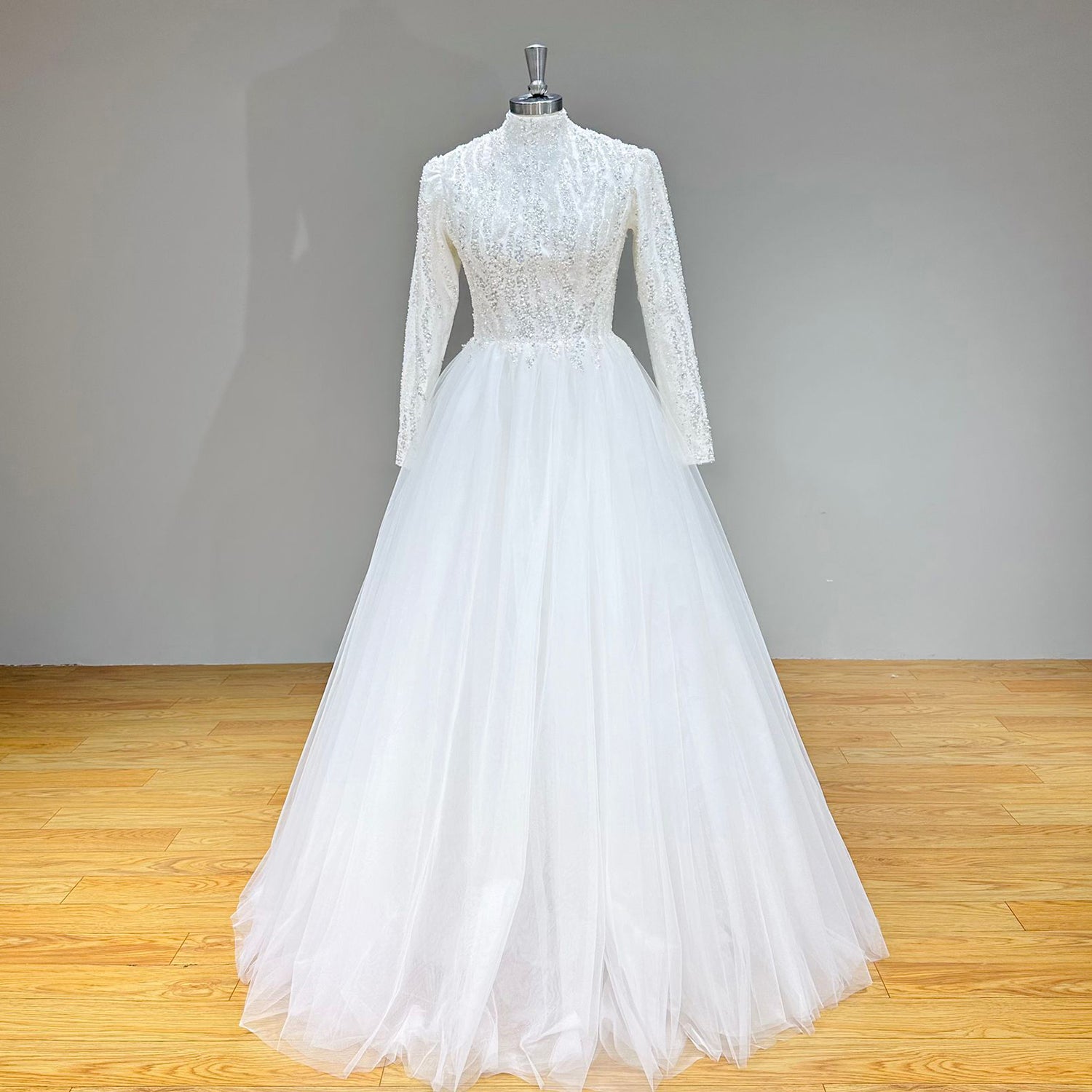 Front view of a vintage-inspired high-neck long-sleeve A-line bridal gown with a shimmering embellished bodice on a dress form.