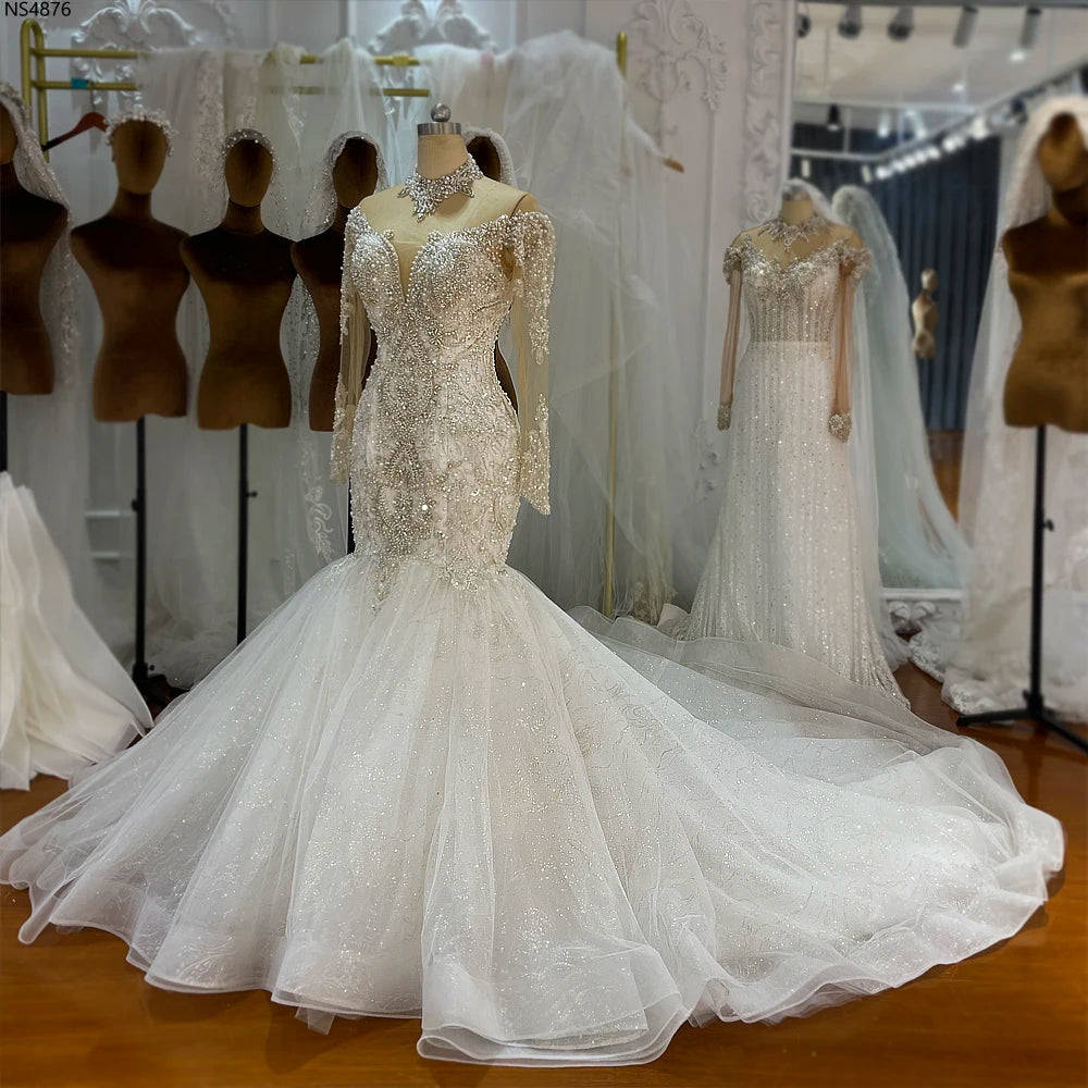 Front view of a luxury mermaid wedding dress on a mannequin, highlighting the off-the-shoulder long sleeves, heavily beaded bodice, and a wide flared skirt.