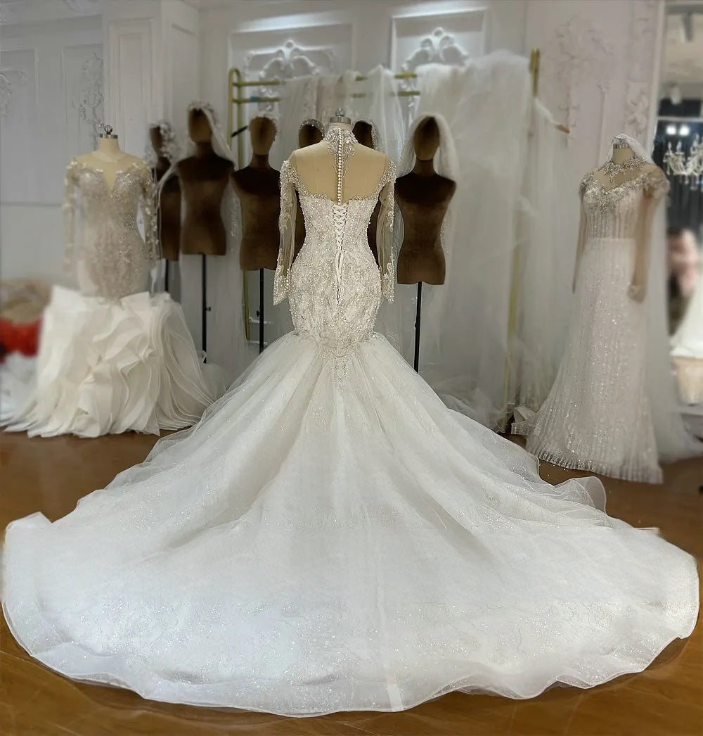 Rear view of a high-quality mermaid bridal gown on a mannequin, displaying a traditional lace-up corset back, long sleeves, and an expansive sparkling train.