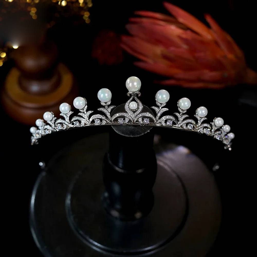 Front view of a high-quality pearl crown CZ tiara displaying arched filigree work and polished white pearls on a black display stand.