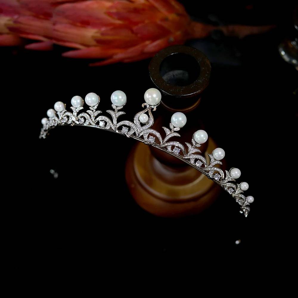 Direct profile perspective of a sparkling wedding hair tiara with round pearl peaks, balanced on a wooden stand.