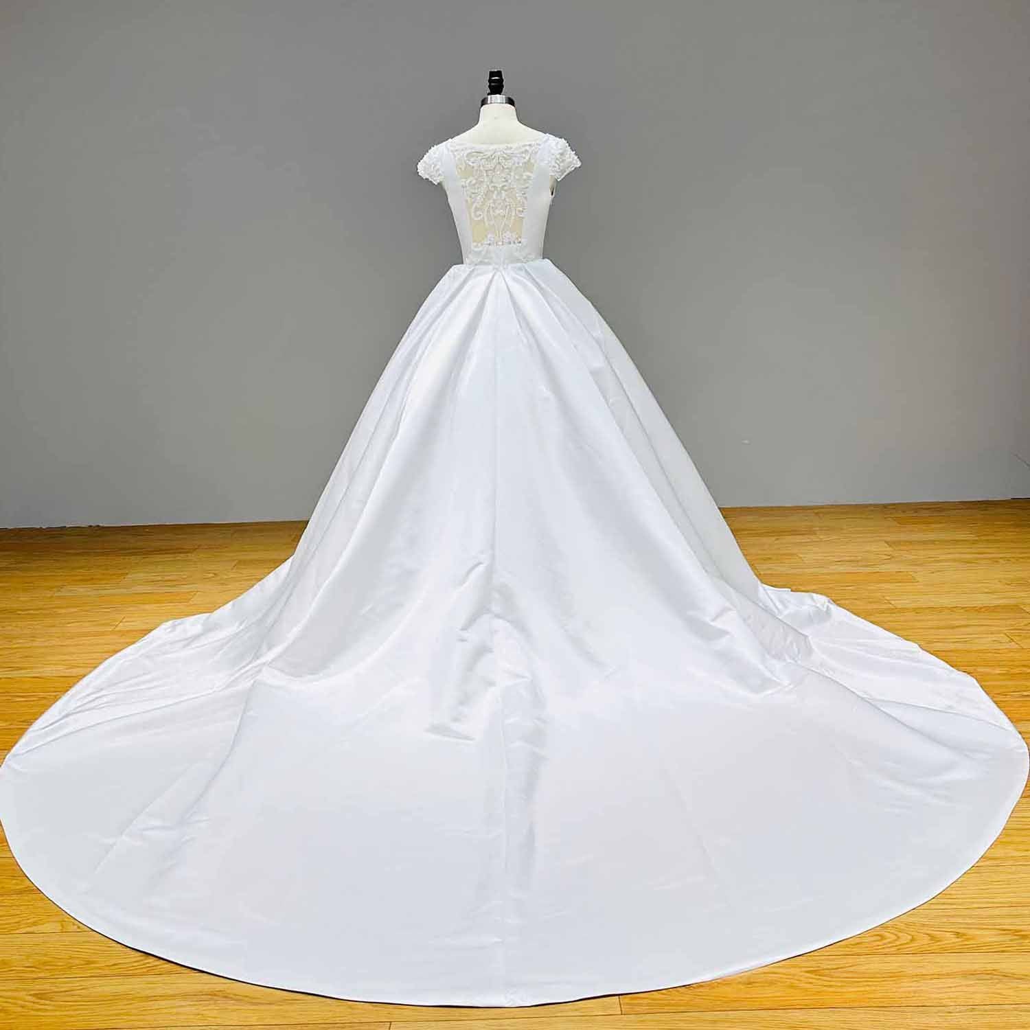 Full-length back studio view of a white satin ball gown wedding dress displaying the expansive, smooth circular cathedral-length satin train.