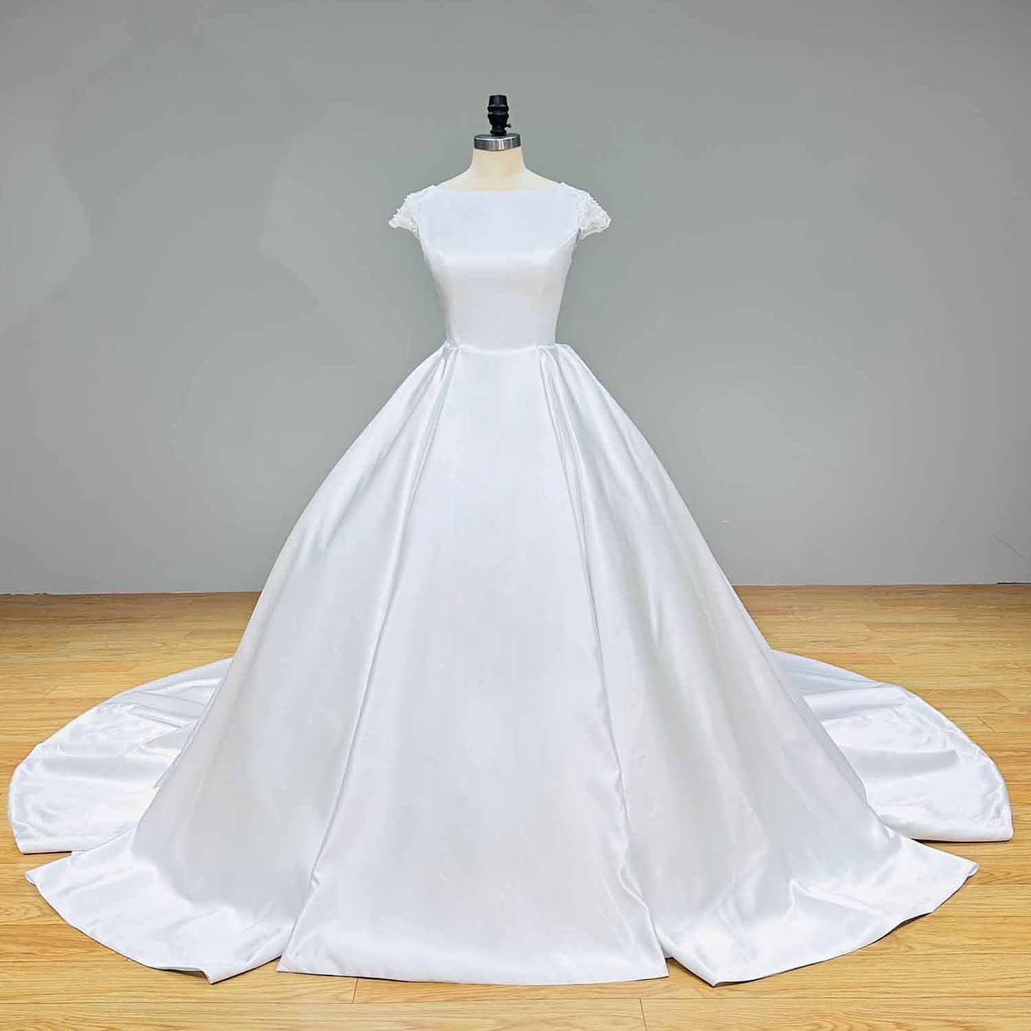 Front studio view of a premium minimalist white satin ball gown wedding dress with a clean boat neck silhouette displayed on a boutique dress form.