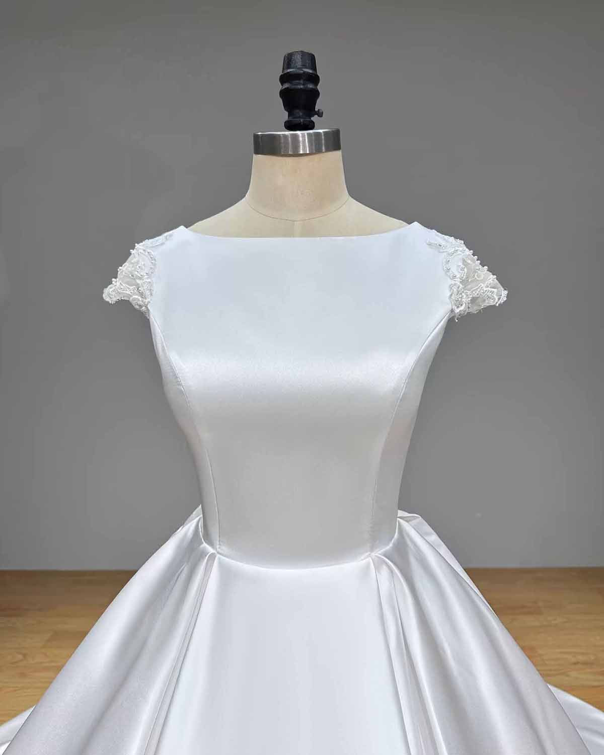 Front close-up of a structured satin bridal bodice showcasing a clean bateau neckline and delicate scalloped lace detailing on the cap sleeves.