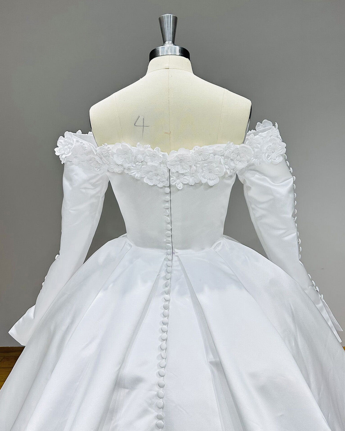 Close-up back view of a satin bridal gown showcasing the intricate 3D floral trim across the shoulders and a classic covered button-down back closure.