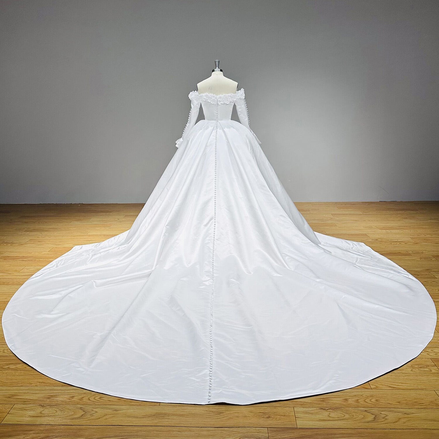 Wide back view of a high-quality satin wedding gown on a mannequin, emphasizing the expansive royal cathedral train and full button detail from waist to hem.