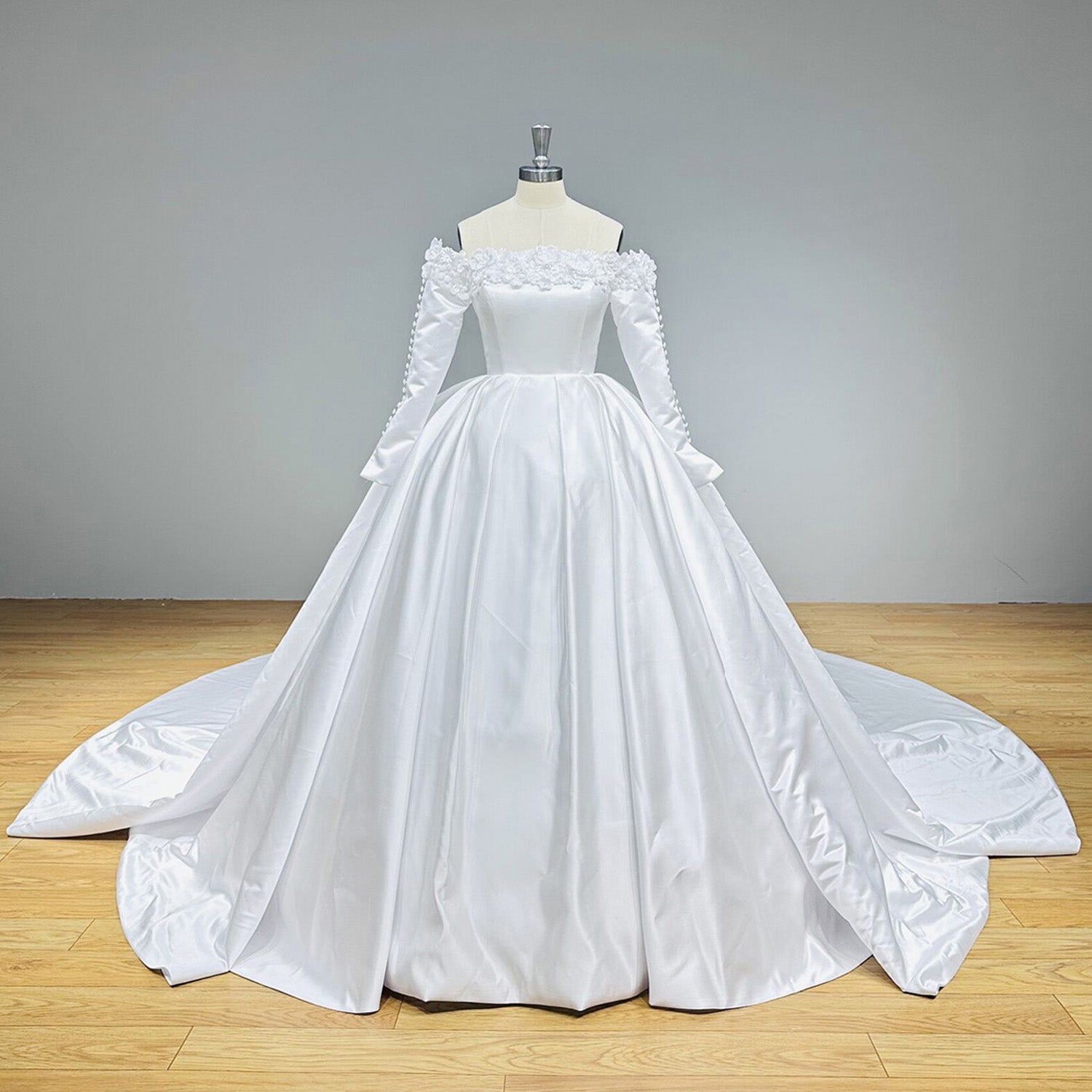 Premium white satin off-the-shoulder ball gown wedding dress with a cinched waist and pleated skirt displayed in a bridal showroom.