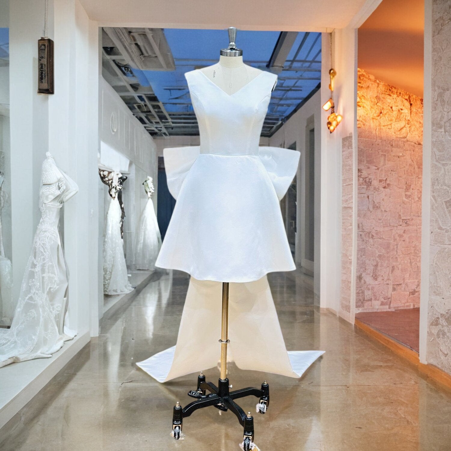 High-quality satin high-low bridal gown featuring a structured sleeveless V-neck top and a flared short skirt silhouette, displayed on a mannequin in a showroom hallway.