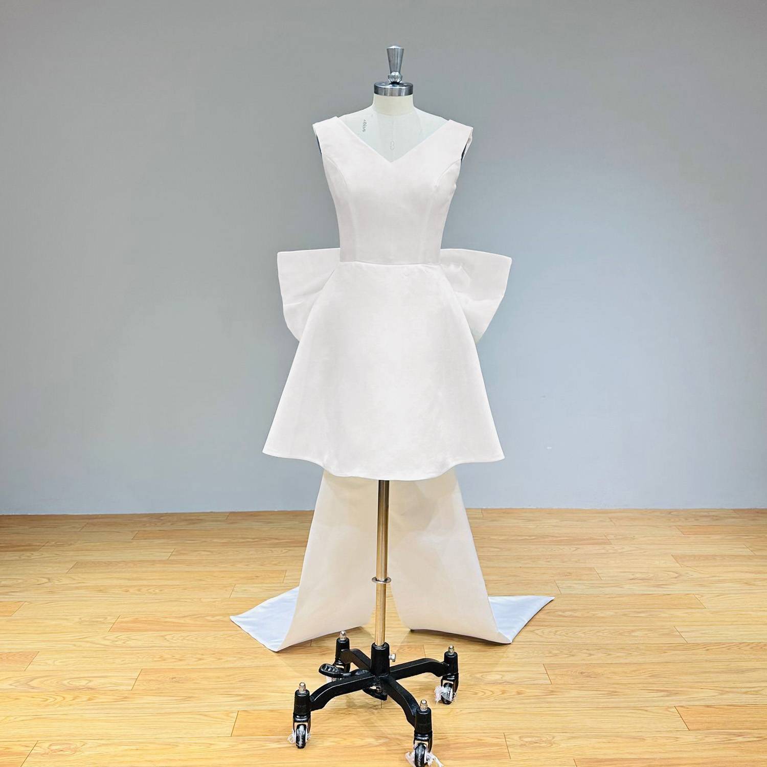 Full-length studio front perspective of the contemporary short white satin bridal gown with an attached overskirt split train on a mannequin.
