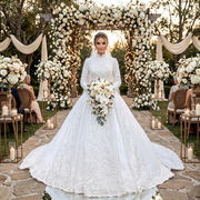 Bride posing in a luxury high-neck beaded long-sleeve princess ball gown wedding dress at an outdoor garden ceremony.
