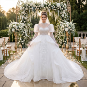 Full-length view of a bride at an outdoor wedding ceremony wearing a luxurious high-neck puff sleeve ball gown featuring intricate beaded lace and a dramatic full skirt.