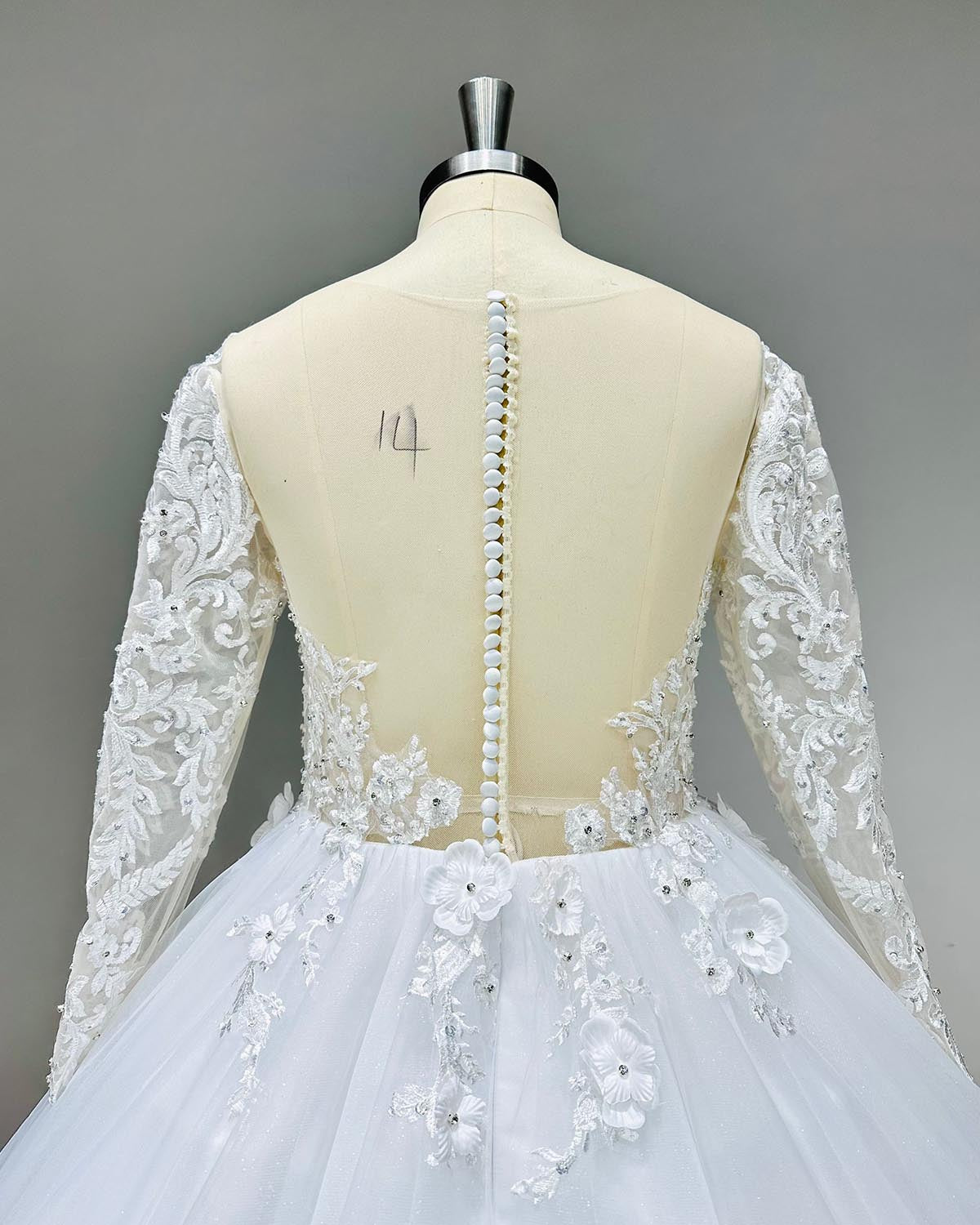 Detailed view of the illusion back with button closure and delicate floral lace on a long-sleeve wedding ball gown.