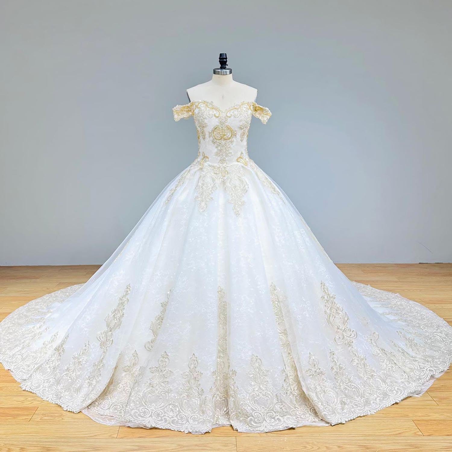 Front view of an off-shoulder white wedding ball gown featuring ornate gold sequin lace and a flattering sweetheart neckline on a mannequin.