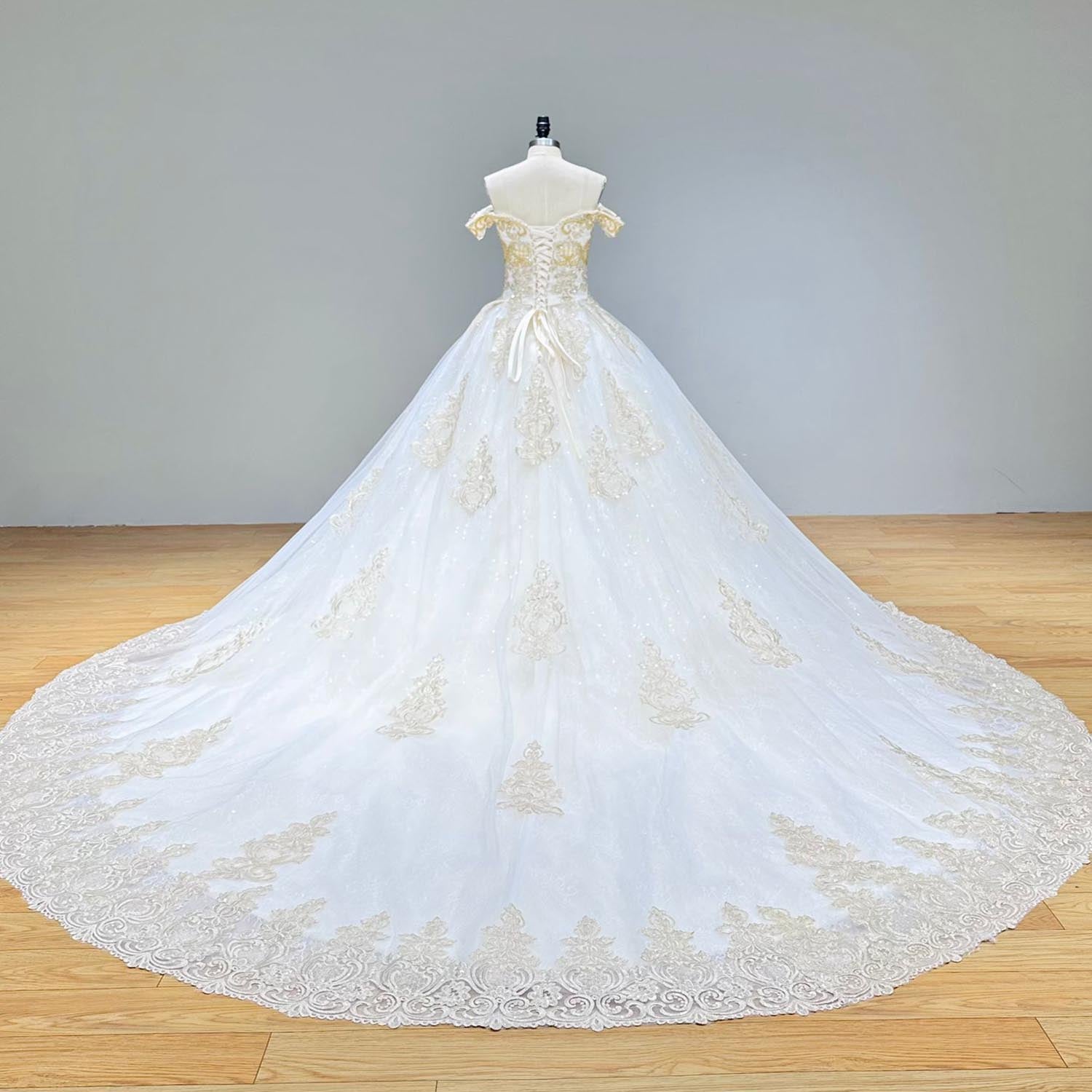 Back view of a white and gold off-shoulder ball gown wedding dress showcasing a dramatic train with intricate lace and bead detailing.