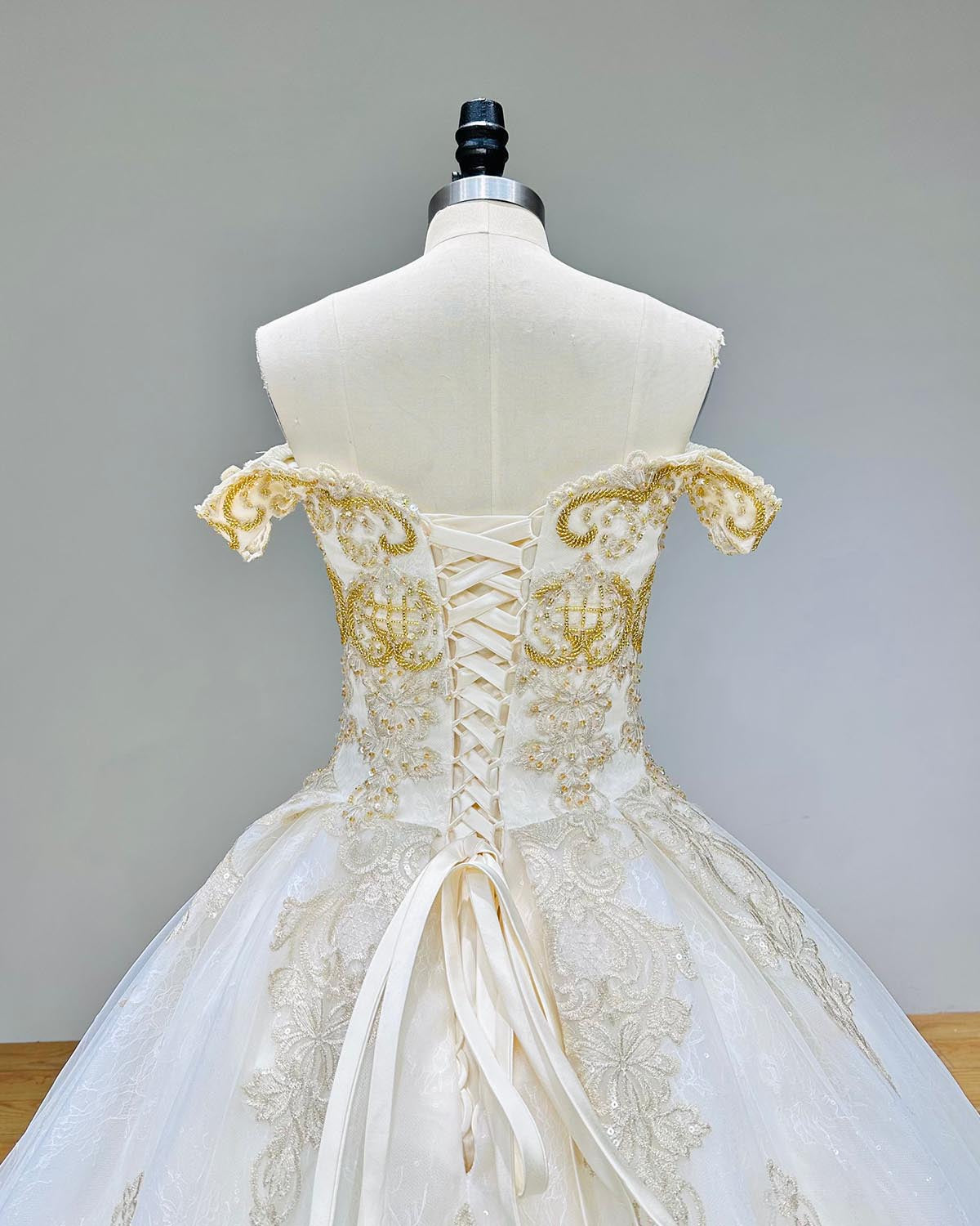 Close-up detail of the sweetheart neckline and ornate gold beadwork on the bodice of an off-shoulder ball gown wedding dress.