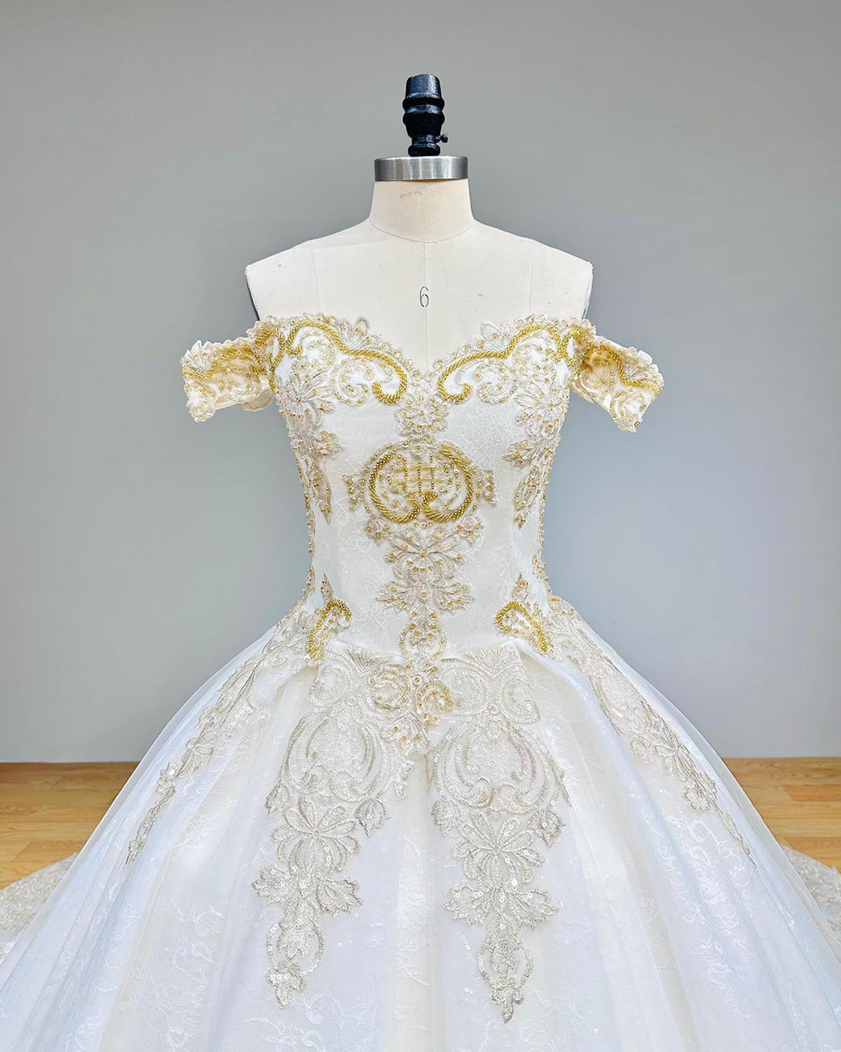 Detailed view of the off-shoulder cap sleeves and gold sequin lace embroidery on a luxury bridal ball gown.