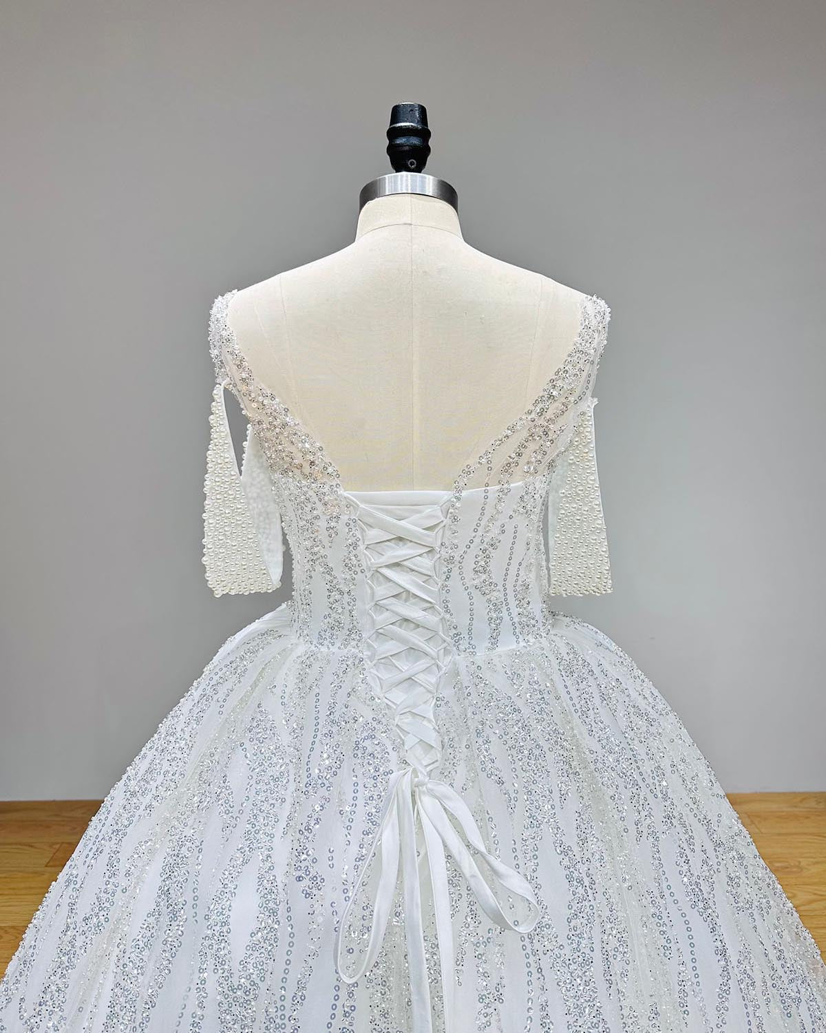 Close-up detail of the lace-up corset back and pearl-studded short sleeves on a bridal ball gown.