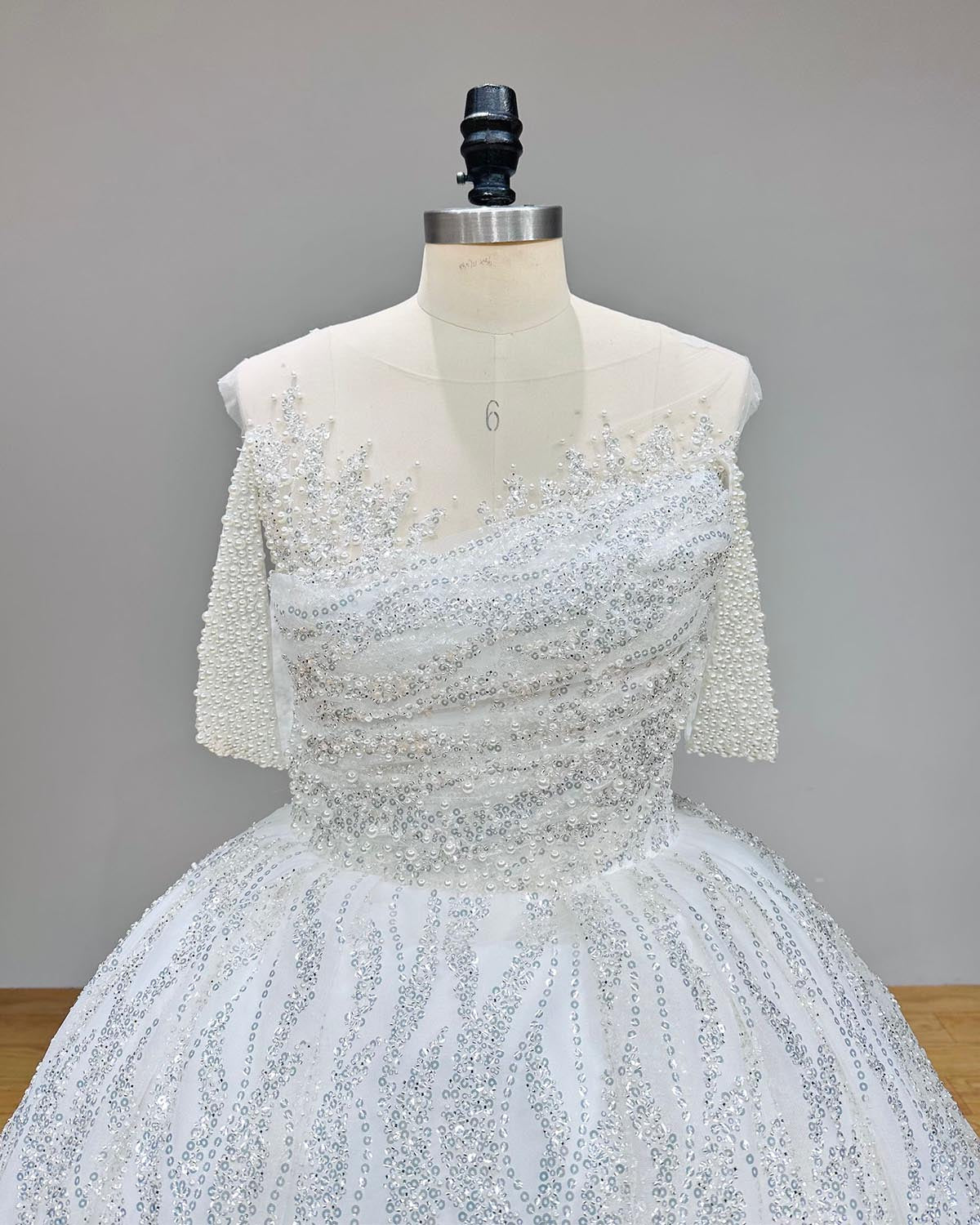 Close-up of the high-neck beaded bodice and pearl-embellished short sleeves on a luxury wedding gown.