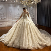 Side view of an elegant model wearing a luxury princess ball gown wedding dress with elegant long sleeves and shimmering crystal beadwork in a grand showroom.