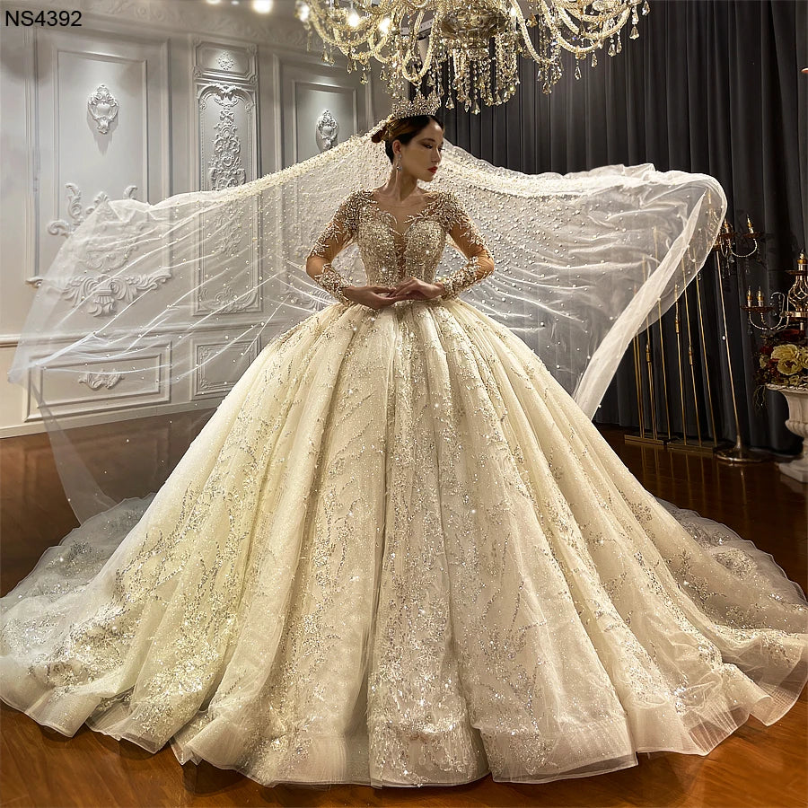 Full-length front view of an ivory luxury ball gown bridal dress featuring a voluminous sparkling skirt and a matching beaded cathedral-length veil.