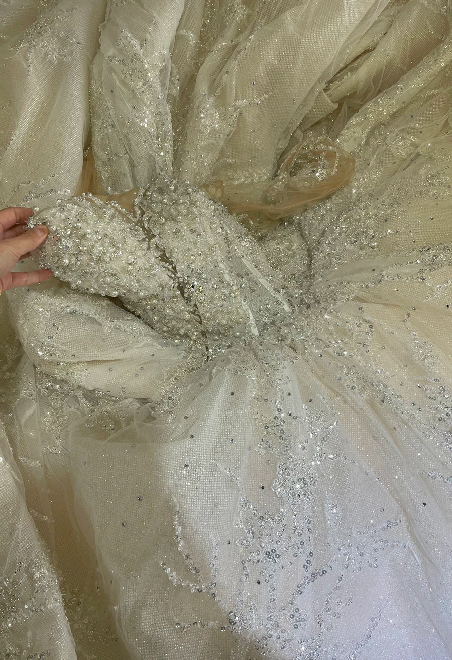 Close-up detail of the heavy beadwork, pearls, and sequin embellishments on the fabric of a high-end luxury princess ball gown.