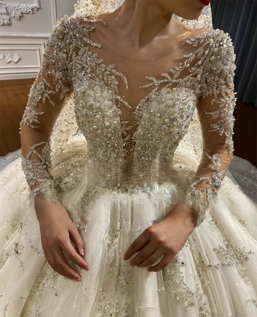 Close-up of the intricately beaded V-neck bodice and sheer long sleeves of a heavy-beaded luxury princess ball gown bridal dress.