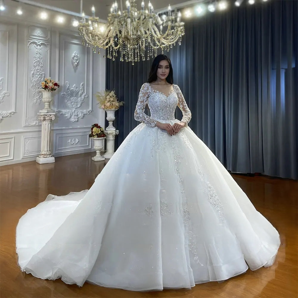 Full front portrait of a bride posing in a hot sale long sleeve wedding dress, featuring an intricate beaded lace bodice and an expansive, pristine white tulle skirt.