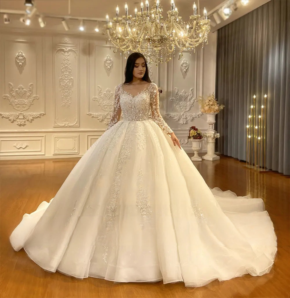 Wide front perspective of an elegant long sleeve ball gown bridal dress, highlighting the majestic spread of the massive cathedral train and delicate floral lace appliques.