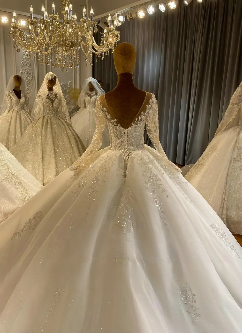 Close-up detail of the back of a luxury long sleeve wedding gown, highlighting the sheer V-shaped open back bordered with intricate floral lace and a classic corset tie.