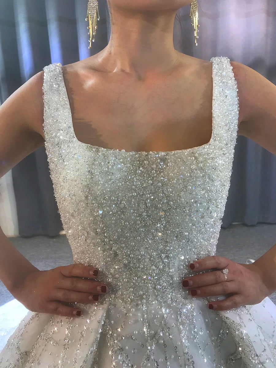 Close-up of a luxury bridal gown bodice showcasing dense hand-sewn pearl beading, crystal embellishments, and intricate shimmering lace details.