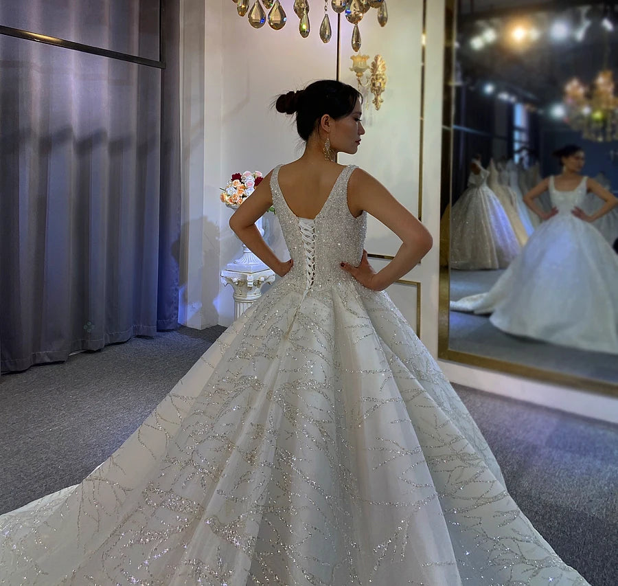 Rear view of a sleeveless bridal gown highlighting a sophisticated V-back with a traditional white lace-up corset closure and a massive, shimmering tulle skirt.