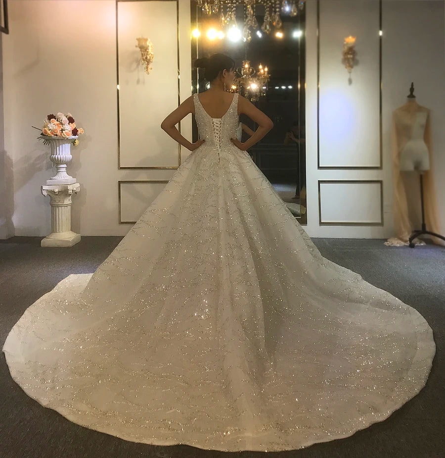 Wide-angle view of a majestic bridal gown with a grand shimmering train and a classic corset back, displayed in a high-end wedding dress showroom.