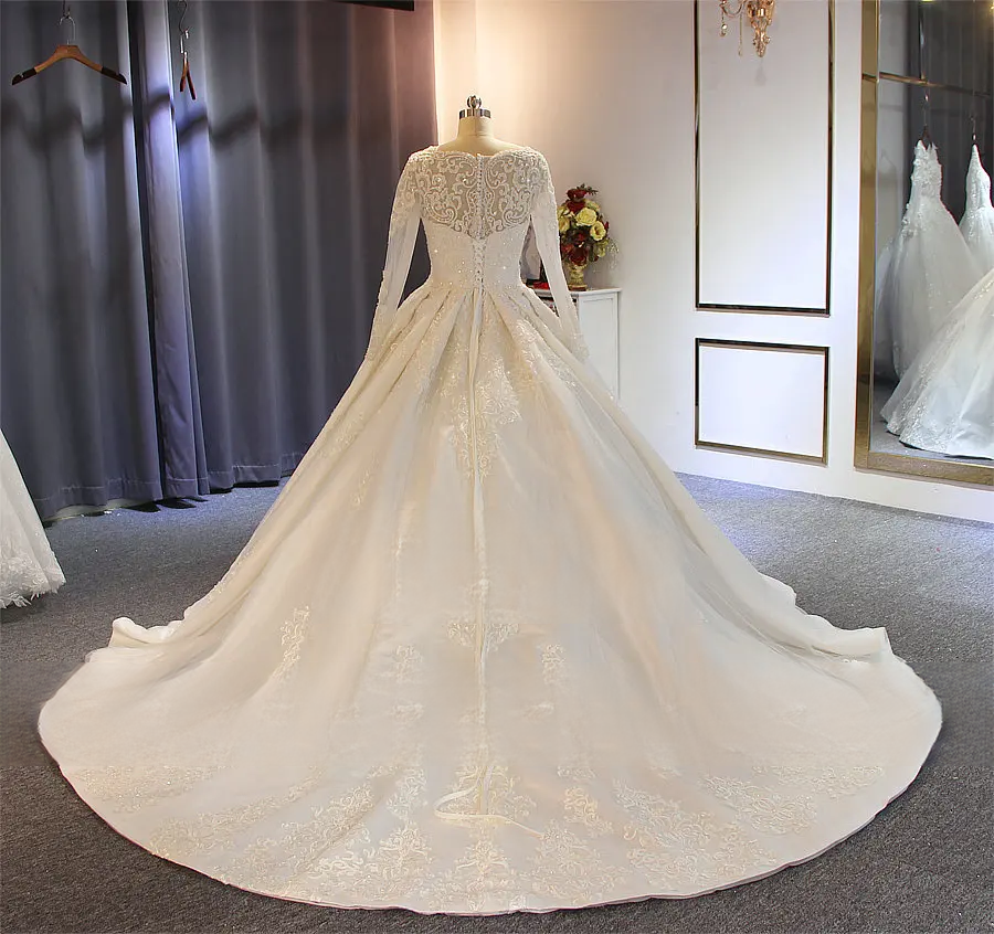 Full-length back view of an elegant wedding dress with a dramatic lace-trimmed train and a sheer illusion back on a mannequin.
