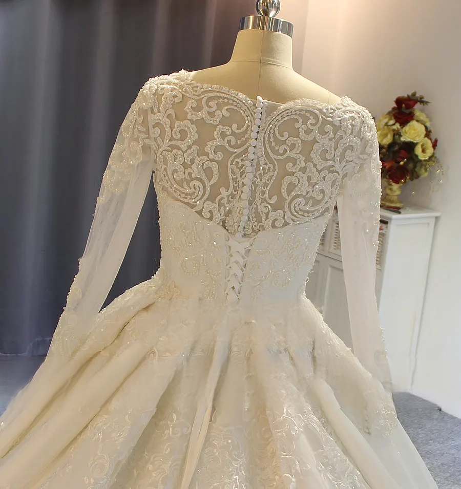 Detailed shot of a bridal gown back featuring delicate pearl button accents, a lace-up corset detail, and sheer floral lace embroidery.