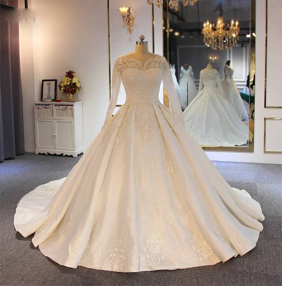 Front-facing view of a hot sale designer bridal gown with a structured beaded bodice, long lace sleeves, and a wide, pleated satin-finish skirt.