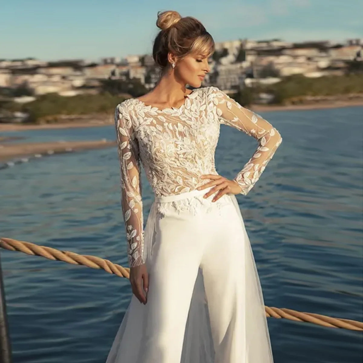 Three-quarter front view of the bridal pantsuit featuring a floral illusion lace bodice, styled with a removable sheer tulle outlayer overskirt attached at the waist.