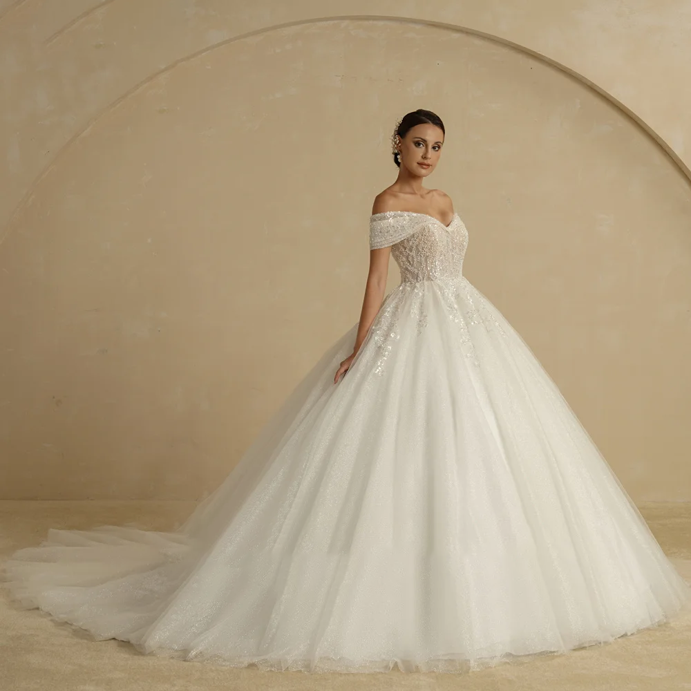 Side profile of a stunning ivory bridal ball gown with a court train, highlighting the off-shoulder sleeves and intricate sparkling lace appliques.