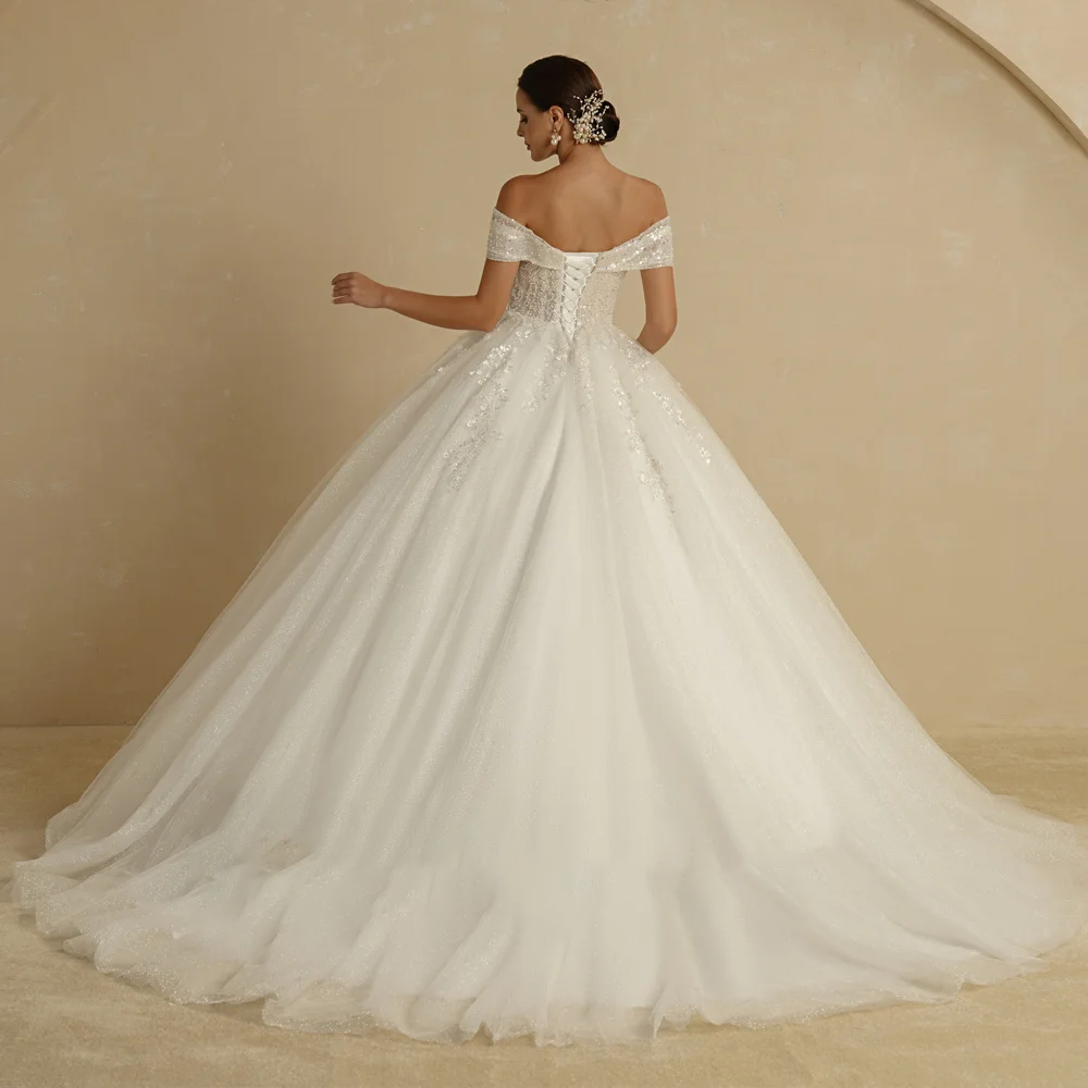 A beautiful bridal gown with off-the-shoulder straps, featuring a glittery skirt and delicate lace appliques, captured in a formal studio setting.