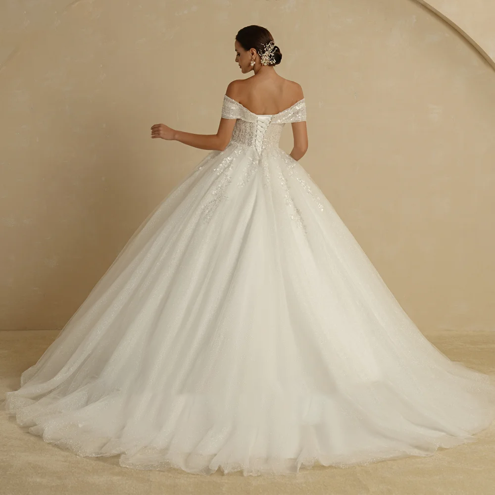 A portrait of a bride wearing an ivory beaded wedding dress with off-the-shoulder sleeves and a princess ball gown skirt.