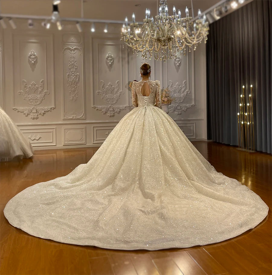 Stunning back view of a luxury ball gown wedding dress with a grand sequined cathedral train and an elegant keyhole back design under a crystal chandelier.