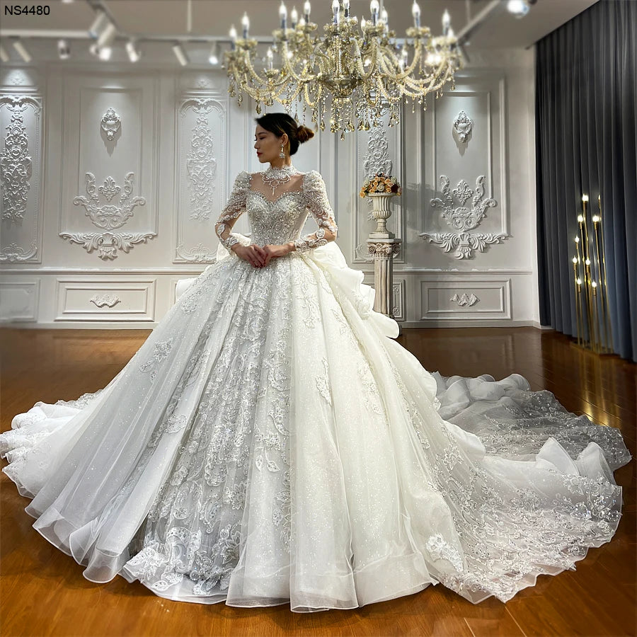 Full front view of a luxury lace applique wedding dress with long sleeves, high neck, and heavy crystal beading featuring a grand royal ball gown silhouette.