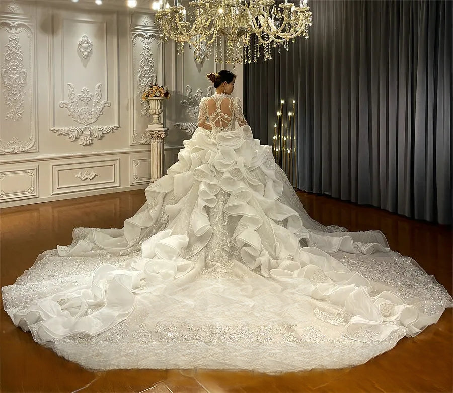 Back view of a luxury bridal gown showcasing a dramatic tiered ruffled royal train and an intricate beaded back design with lace appliques.
